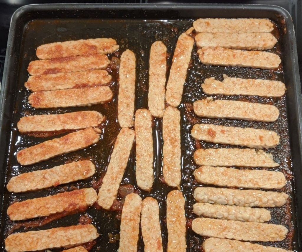 Tempeh strips, covered in marinade, ready to bake